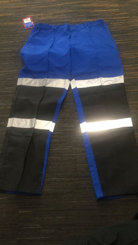 Pair of blue and black work pants with reflective white safety strips, laid flat on wooden surface with price tag attached