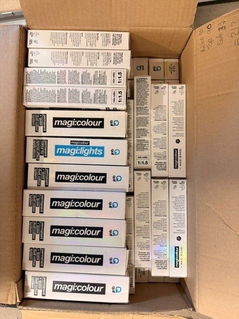 Cardboard box containing multiple tubes of Magi:colour paint and instruction manuals organized in rows