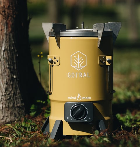 Yellow Gotral camping stove with black handles and control dial, positioned outdoors next to a tree