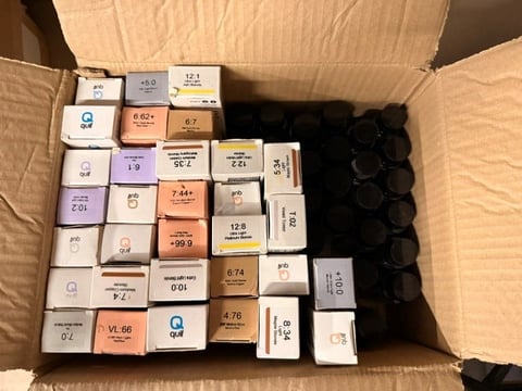 Open cardboard box filled with various labeled cosmetic and beauty product samples arranged in rows