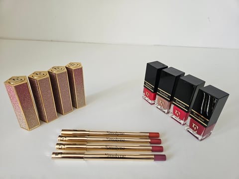 Collection of cosmetics including rose gold lipsticks with burgundy shades, black nail polishes in pink and purple tones, and matching lip liner pencils arranged on white surface.