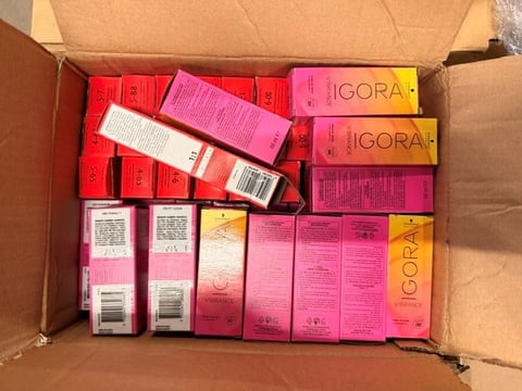 Cardboard box filled with cosmetic products in red and pink packaging, including IGORA branded hair care items and beauty products