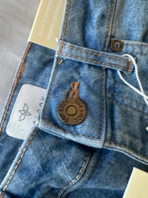 Close-up of new blue jeans with brand label, white drawstring, and leather button detail