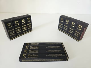 Four black Emolyne skincare boxes displayed in a set arrangement, with spines facing forward and gold lettering on white surface