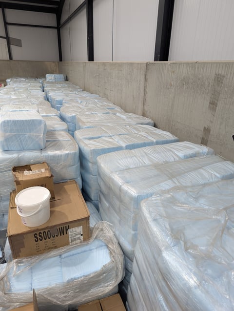 Multiple wrapped packages and supplies stored in an industrial warehouse space with concrete walls
