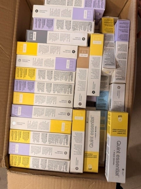 Cardboard box filled with various cosmetic and skincare product boxes in yellow, purple, and white packaging