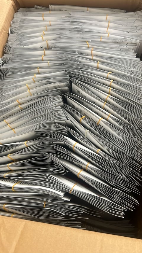Large stack of organized document bundles with yellow rubber bands in a cardboard box