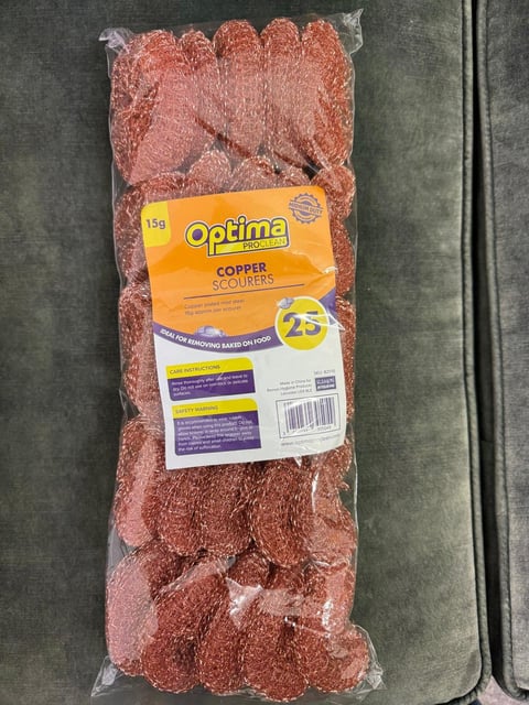 Package of Optima copper scourers in clear plastic wrapping on a dark surface