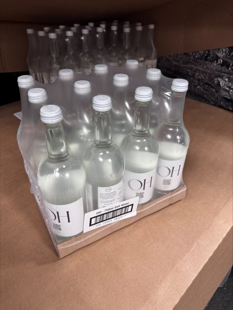 Case of clear glass bottles with white caps containing liquid, arranged on cardboard packaging on a wooden surface