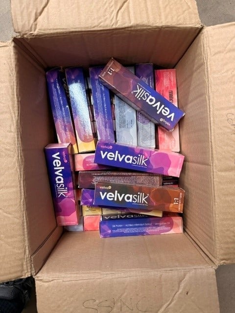 Cardboard box containing multiple Velvasilk hair care product boxes in purple, pink, and brown packaging