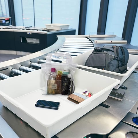 Organized luggage and personal items displayed on white trays at an airport security checkpoint