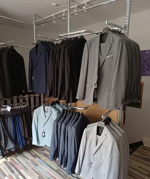 Retail clothing display with blazers and suits organized on metal shelving and racks in shades of navy, black, gray, and light blue