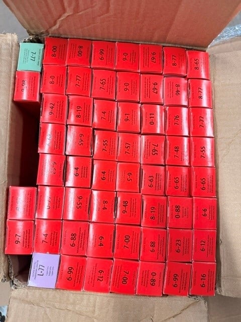 Overhead view of red capacitors arranged in rows inside a cardboard box with one blue label visible